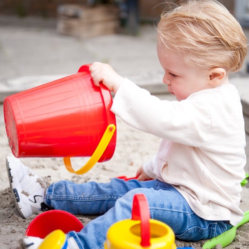 peuter speelt met een rode emmer in de zandbak op het kinderdagverblijf