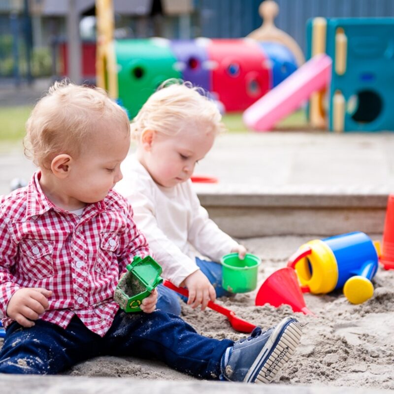 twee peuters spelen buiten in de zandbak op het kinderdagverblijf