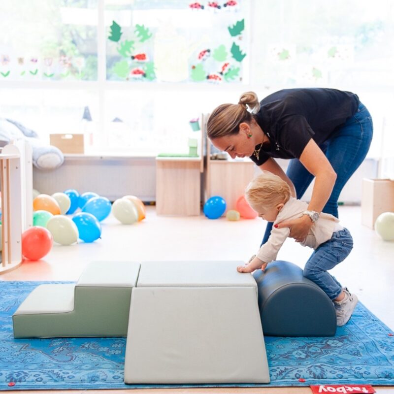 pedagogisch medewerker helpt baby kruipen op een mat in het kinderdagverblijf