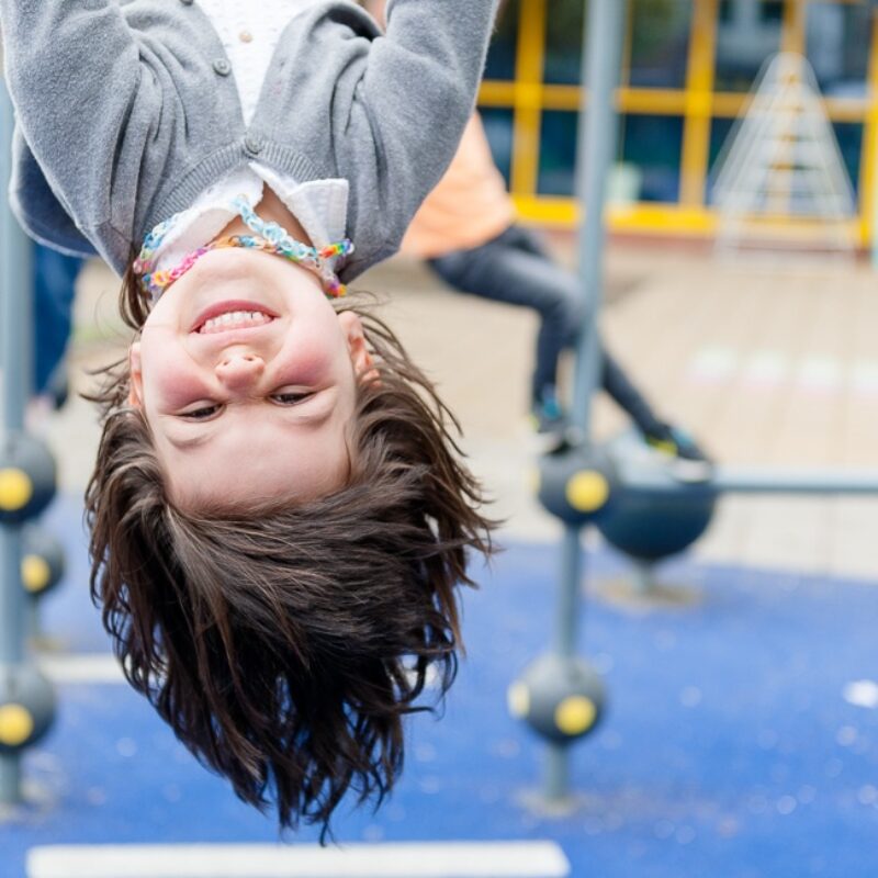 kind hangt lachend aan een klimtoestel van de buitenschoolse opvang