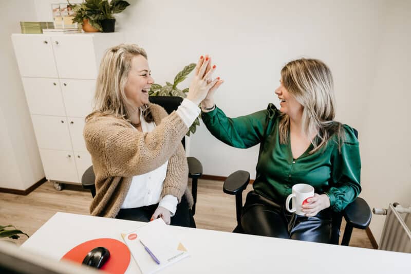 twee medewerkers geven elkaar een high five achter het bureau