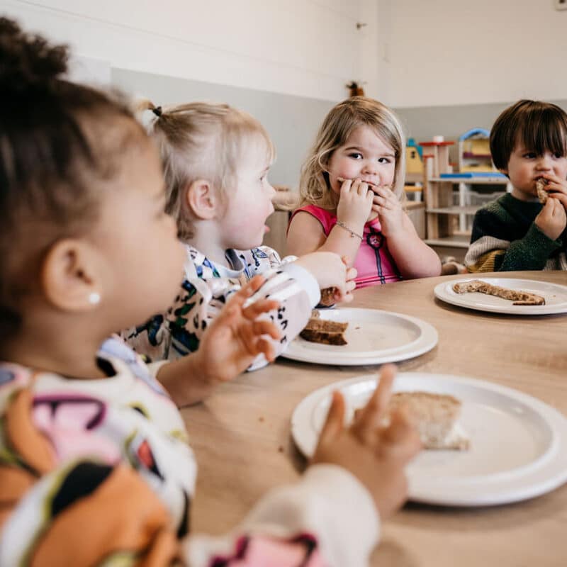vier peuters eten broodjes aan tafel op het kinderdagverblijf